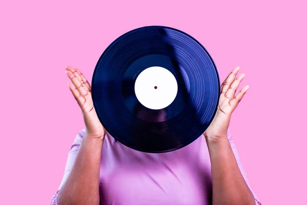 Hipster lady with cool dreadlocks pigtails showing old fashion school vinyl in pink studio background — Stock Photo, Image