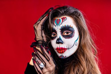 Kırmızı stüdyo arka planında Calavera Catrina kostümü giymiş Meksikalı genç bir kadın.