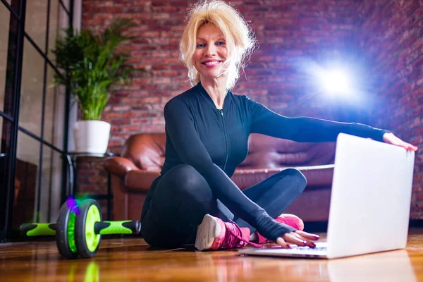 Actieve oudere vrouw opwarmen, benen strekken oefeningen thuis, kijken naar online lessen op laptop — Stockfoto