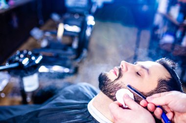 Arap yakışıklı sakallı adam berber dükkanında saçını kestiriyor.