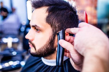 Arap yakışıklı sakallı adam berber dükkanında saçını kestiriyor.