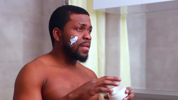 Hispánský africký muž hydratuje svůj obličej doma v koupelně — Stock video