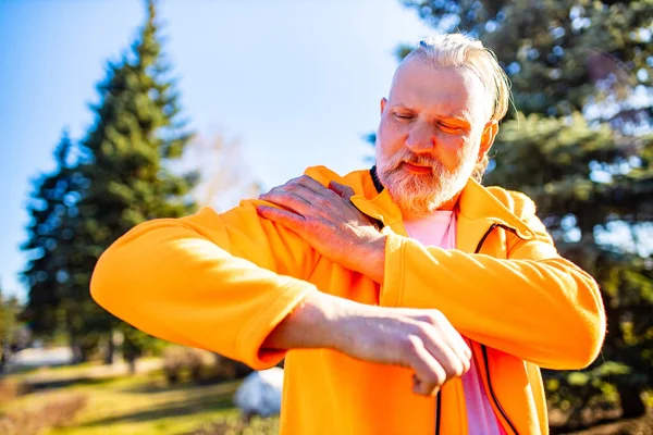 Hombre mayor en ropa deportiva naranja haciendo estiramiento calentamiento al aire libre día soleado en el bosque solo —  Fotos de Stock