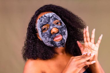 Kahverengi arka planda, yüzünde baloncuk maskesi olan genç bir kadın.