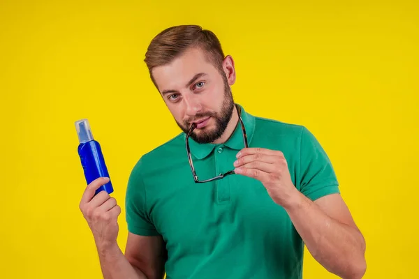 Человек держит бутылку крема для загара в студии желтый фон — стоковое фото