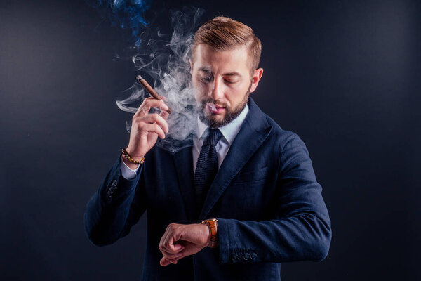 Портрет привлекательного бизнесмена с сигарой на черном фоне студии