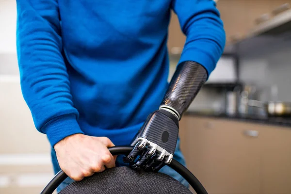 Giovane uomo con le mani cyborg muovendo la sedia e seduto in cucina a casa — Foto Stock