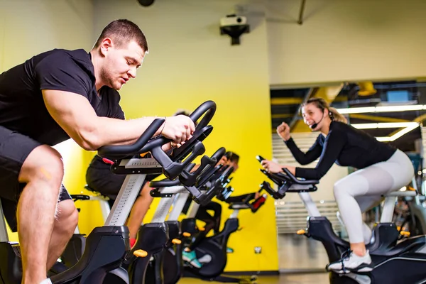 Quatro pessoas positivas autênticas com treinamento de idade de instrutor de programa de grupo em bicicletas de exercício na sala de ciclismo, mantendo uma distância segura um do outro — Fotografia de Stock