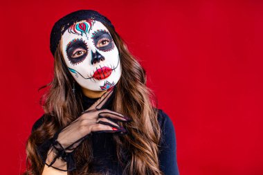 Meksika 'ya gitmek için yüzünde boyalı kafatası olan bir kadın. Kırmızı stüdyo arka planında geleneksel Meksika ritüeli.