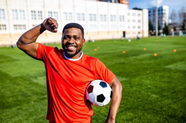 Mutlu çok kültürlü İspanyol futbolcu gülümsüyor ve açık hava güneşli bir günde kırmızı spor takım elbise giyiyor.