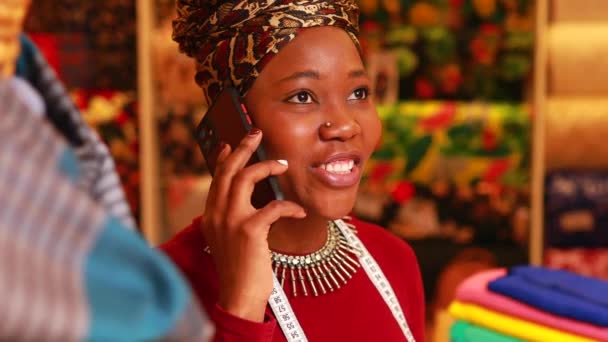 Tanzanian mujer con serpiente impresión turbante sobre escuchar a trabajar en telas tienda — Vídeo de stock