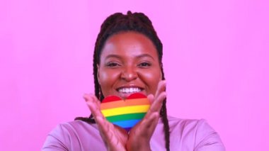 Pembe stüdyo arka planında kalbi olan Afro-Amerikalı bir kadın.