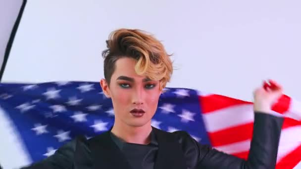 Retrato de close-up de um jovem com um batom envolto em bandeira americana fundo branco — Vídeo de Stock
