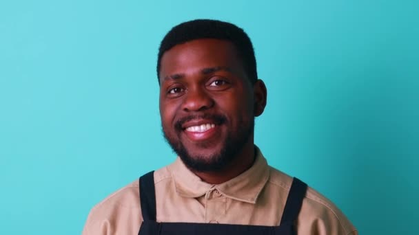 Šťastný latin muž v bavlněné košili mravenec černá zástěra v modrém studiu při pohledu na kameru a dobrý pocit — Stock video