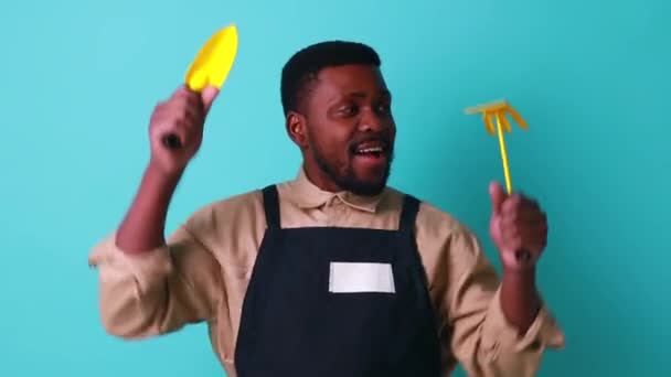 Бразильский садовник мужчина держит сад желтые предметы в студии синий фон — стоковое видео