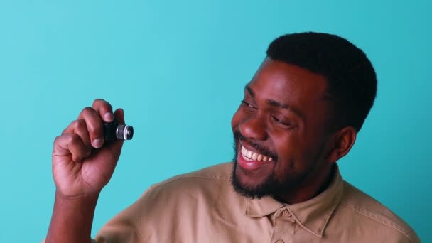 Mini camera in hand of african american man in blue studio — Stock Video