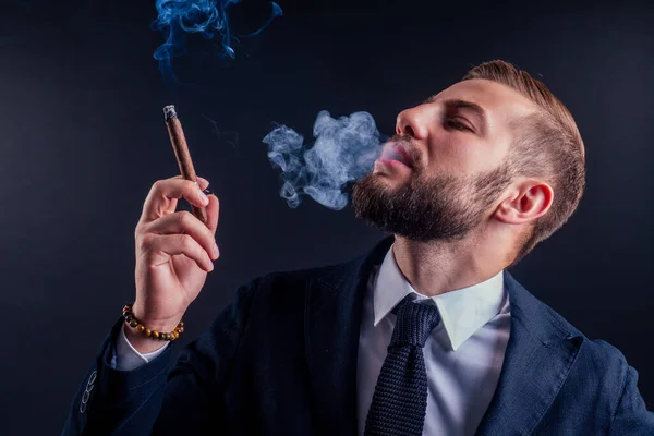 Retrato de un atractivo hombre de negocios con un cigarro en un estudio de fondo negro — Foto de Stock