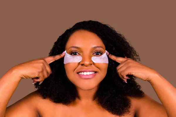 Ελκυστική γυναίκα εφαρμογή αντι-κόπωση κάτω από τα μάτια μάσκα σε στούντιο καφέ φόντο — Φωτογραφία Αρχείου