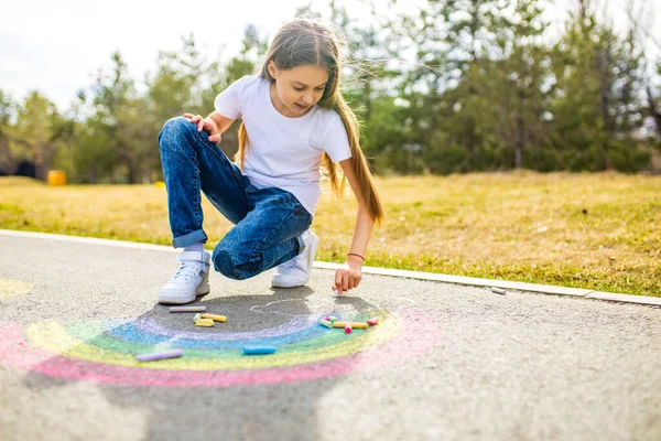 Genç kız yaz günü asfalta gökkuşağı renkli tebeşir çiziyor. — Stok fotoğraf