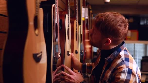 Rusovlasý zázvorový muž si vybírá kvalitní akustickou kytaru v kytaře — Stock video
