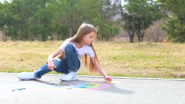 Teenage girl drawing a rainbow colored chalk on the asphalt on summer day — Stock Video