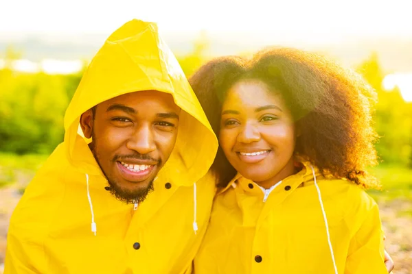 Africano americano esposa y marido en amarillo impermeable con un capucha sensación feliz al atardecer al aire libre verano lluvia gota — Foto de Stock