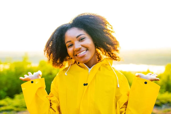 afro amrican woman curly hair wear yellow raincoat and looking at camera outdoor sunset lights