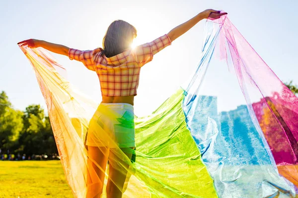 Mujer joven mostrando arco iris gran bandera al aire libre en el parque vacío verano — Foto de Stock