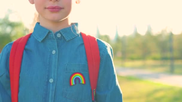 Flicka i denim t-shirt med regnbåge symbol bära ryggsäck i sommar park utomhus. — Stockvideo