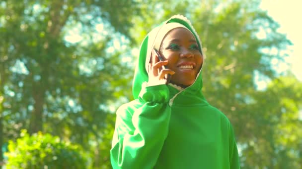 Mujer árabe hispana latina en vestido verde musulmán con maquillaje moderno brillante y piercing en la nariz hablando por teléfono — Vídeos de Stock
