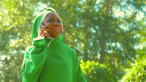 Mujer árabe hispana latina en vestido verde musulmán con maquillaje moderno brillante y piercing en la nariz hablando por teléfono — Vídeo de stock
