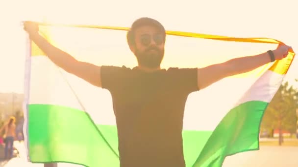 노을 골 그 라이트에서 검은 색 면 티셔츠를 입은 인도 남자가 여름 공원에서 국기를 흔들고 있습니다.. — 비디오