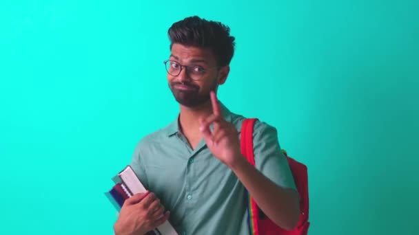 Schöner junger bärtiger indischer Mann mit Brille in blauem Baumwoll-T-Shirt mit orangefarbenem Regenbogenrucksack im Studiohintergrund — Stockvideo