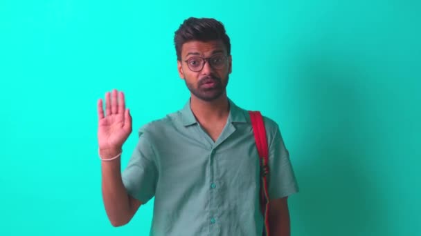 Indio estudiante hombre sentirse feliz mirando cámara usar gafas de ojo y naranja mochila y decir hola con la mano en azul estudio — Vídeos de Stock
