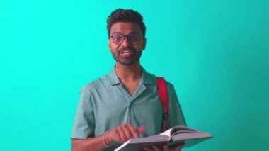 Stüdyo arka planında turuncu gökkuşağı sırt çantalı mavi pamuklu gözlüklü yakışıklı, ayı gözlü Hintli adam.