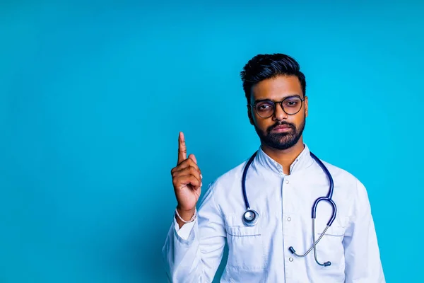 Indický vousatý kardiolog muž s očima brýle v bílém lékařském kabátě se stetoskopem v modrém studiu pozadí — Stock fotografie