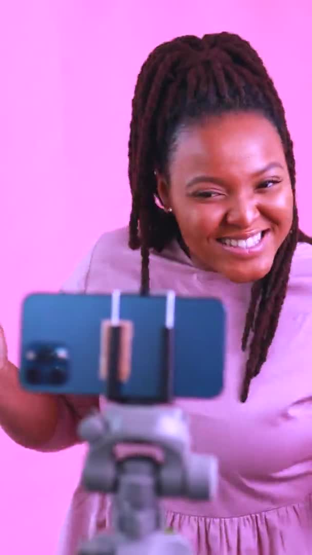 Темнокожая женщина смеется и снимает истории в социальных сетях на фоне розовой стены — стоковое видео