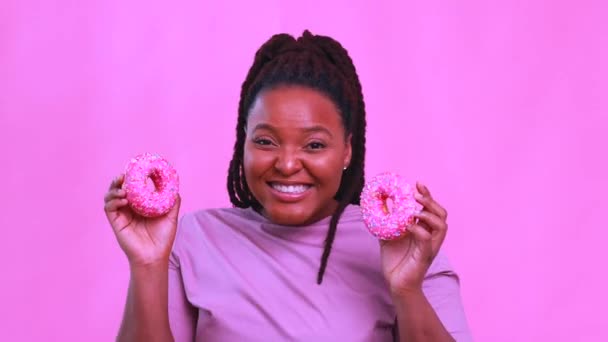 Мультикультурна жінка тримає смачний солодкий пончик на рожевому студійному фоні — стокове відео