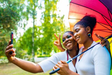 İki Afro-Amerikalı kadın, yaz parkında parlak bir erkekle Wtite elbisesiyle evliliklerini kutluyorlar.