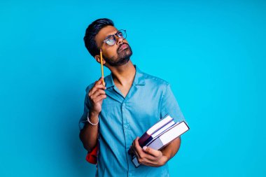 Hintli öğrenci ilham verici bir fikir. Mavi stüdyoda bir kalem tutan gözlük takıyor.