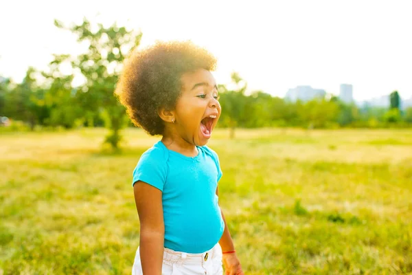 Linda niña afroamericana en algodón camiseta azul en el parque de primavera al atardecer pelo rizado —  Fotos de Stock