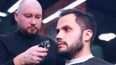 Berber dükkanında berbere saçını kestiren İspanyol sakallı adam.