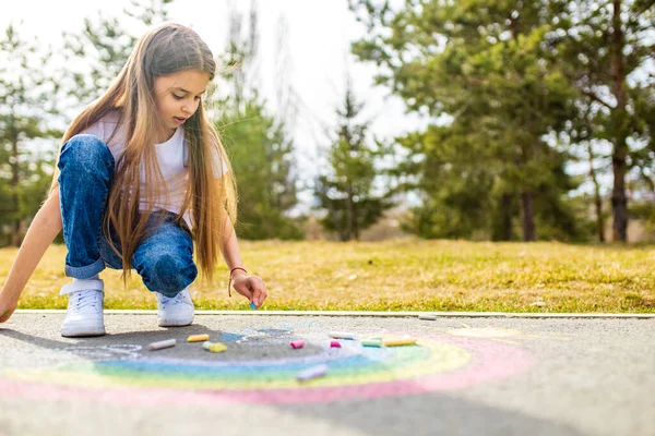 Teenager-Mädchen zeichnet an einem Sommertag eine regenbogenfarbene Kreide auf den Asphalt — Stockfoto