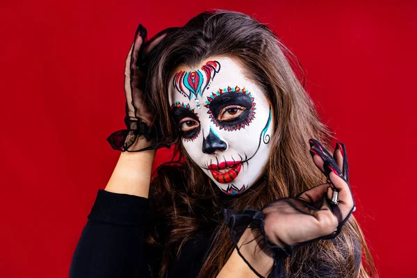 Kvinna med målade skalle på hennes ansikte för Mexiko D a de Muertos mexikanska traditionell ritual i röd studio bakgrund — Stockfoto
