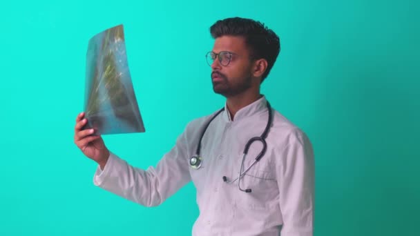 Médico indio mostrando imagen de rayos X de película ósea de pecho en baclground estudio azul — Vídeos de Stock