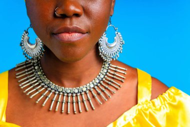 Sarı ipek türbanlı güzel bir Afrikalı kadın gümüş yakalı ve küpeli, mavi arka planda burun piercingli.