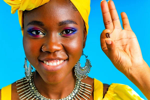 Schöne afrikanisch-amerikanische Frau mit gelbem Turban auf dem Kopf zeigt frischen Kaffee und im Studio blauen Baclground — Stockfoto