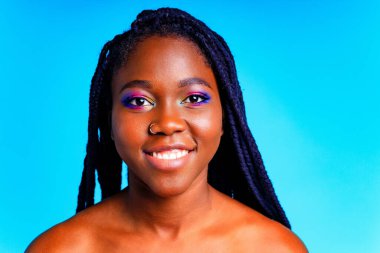 Gökkuşağı makyajlı ve mavi stüdyo arka planında uzun kirpikli bir kadın.