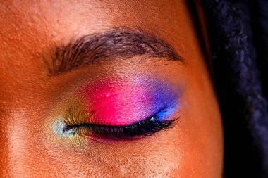 Gökkuşağı makyajlı ve mavi stüdyo arka planında uzun kirpikli bir kadın.