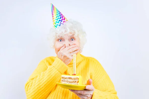 Femme plus âgée avec un cadeau porter pull jaune et chapeau de corne sur un fond blanc plaque de maintien avec gâteau avec feux d'artifice — Photo